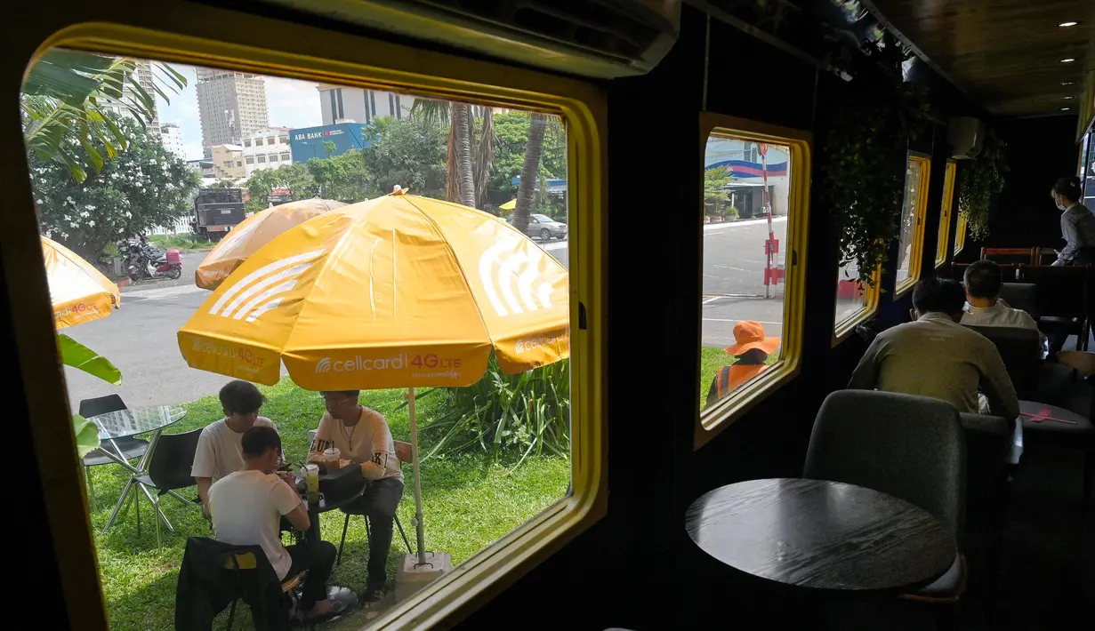 Foto yang diambil pada 31 Mei 2021 menunjukkan orang-orang duduk di luar gerbong kereta yang diubah menjadi kafe di stasiun kereta api di Phnom Penh. Gerbong kereta diubah menjadi kafe setelah selama pandemi corona sebagian besar perjalanan kereta api di Kamboja dihentikan. (TANG CHHIN Sothy/AFP)