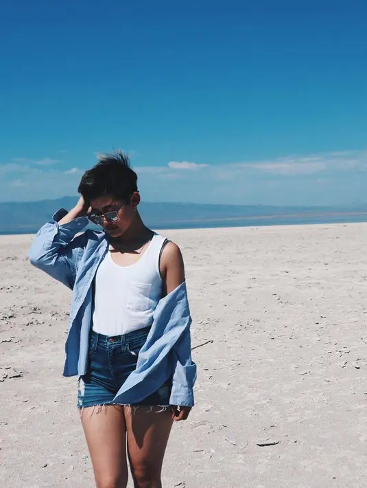 Masih di pantai, kali ini adik Gracia Indri ini memakai denim short pants dengan atasan putih dan kemeja denim yang digunakan sebagai outernya.  (Instagram/giselacindy12)