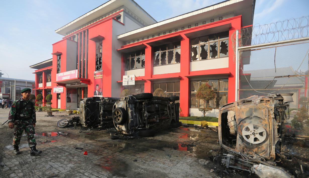 Prajurit TNI melintasi bangkai mobil yang rusak dampak kerusuhan di Lapas Narkotika Kelas III Langkat, Sumatera Utara, Kamis (16/5/2019). Akibat peristiwa kerusuhan yang dilakukan para narapidana di Lapas itu mengakibatkan tiga mobil petugas rusak terbakar dan ratusan napi melarikan diri. (AP Photo)