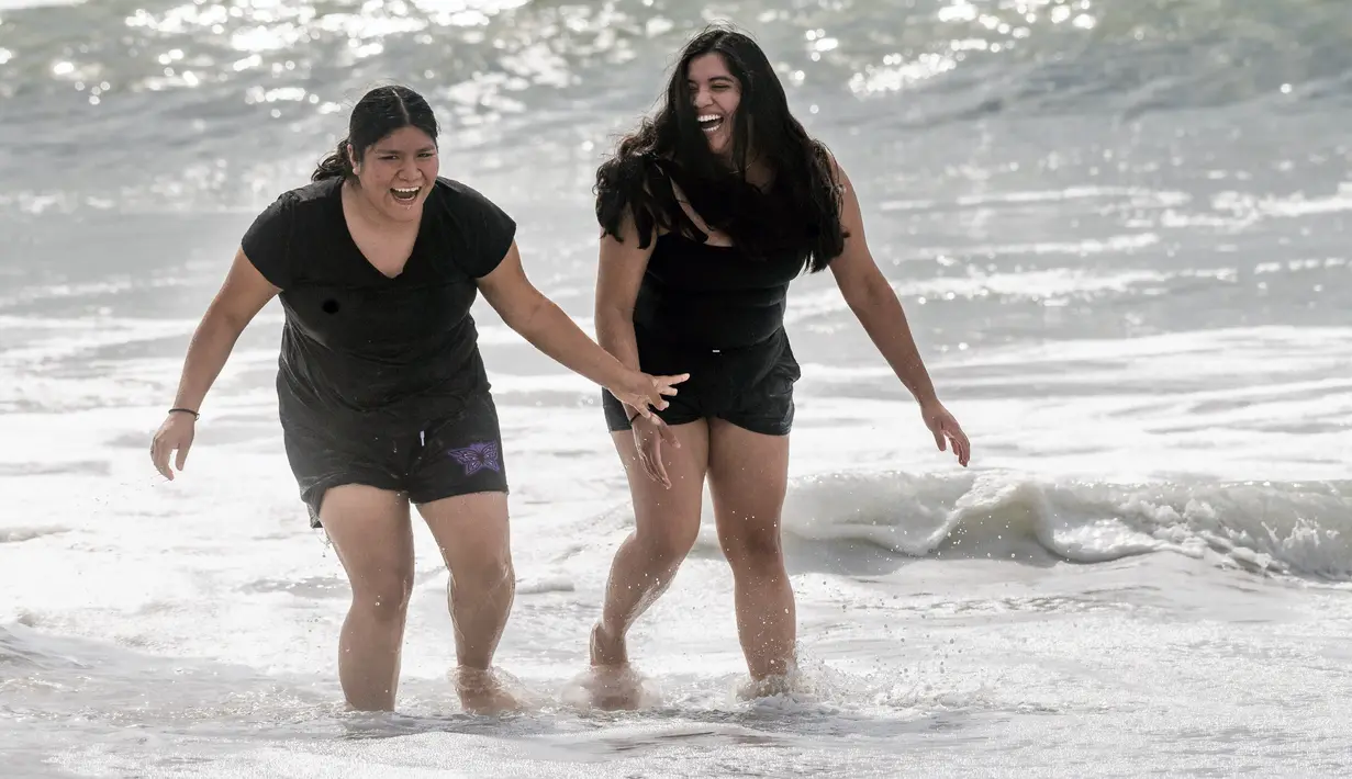 Dua wanita saat masuk ke air di Huntington Beach, California, Senin (11/10/2021). Pantai Huntington membuka kembali garis pantainya setelah hasil pengujian air kembali dengan jumlah racun terkait minyak yang tidak terdeteksi di air laut. (Paul Bersebach/The Orange County Register via AP)