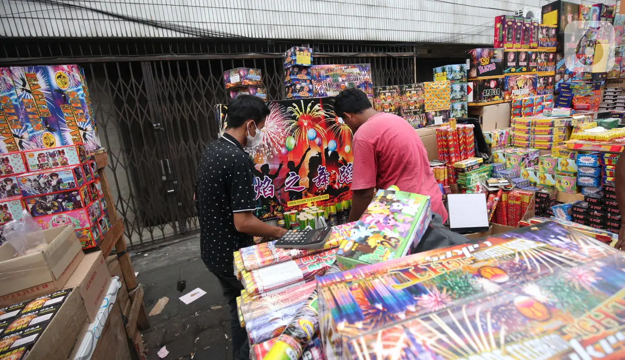 Pedagang melayani pembeli kembang api di Pasar Asemka, Jakarta, Kamis (30/12/2021). Meski Larangan Tahun Baru 2022 diberlakukan untuk membatasi mobilitas, namun masih banyak warga yang berburu kembang api baik untuk dijual maupun digunakan sendiri. (Liputan6.com/Johan Tallo)
