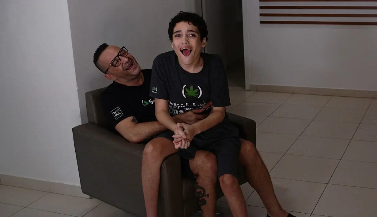 Gabriel Guerra (kanan) bersama ayahnya Ricardo Guerra di Rio de Janeiro, Brasil, 20 September 2021. Ricardo memberi ganja obat kepada Gabriel dalam bentuk tetesan untuk membantu anaknya dari autisme berat dan cerebral palsy. (CARL DE SOUZA/AFP)