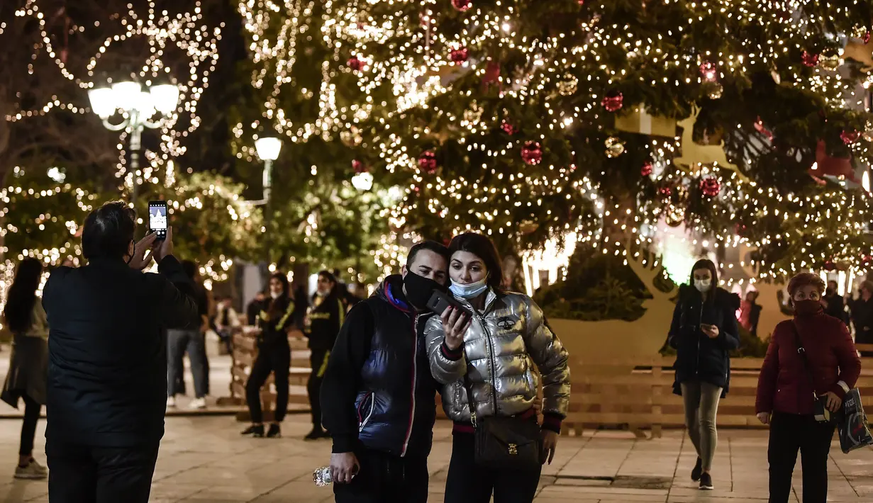 Orang-orang berfoto di alun-alun Syntagma yang diterangi dekorasi Natal di pusat kota Athena, Yunani pada 21 Desember 2020. Yunani akan merayakan musim Natal di bawah langkah-langkah penguncian wilayah atau lockdown COVID-19 hingga 7 Januari 2021 mendatang. (LOUISA GOULIAMAKI/AFP)