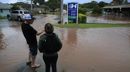 Orang-orang berdiri di tepi air banjir di sepanjang Jalan Haleiwa di Hawaii (9/3/2021). Hujan deras telah menggenangi beberapa bagian Hawaii selama beberapa hari terakhir. (Jamm Aquino/Honolulu Star-Advertiser via AP)