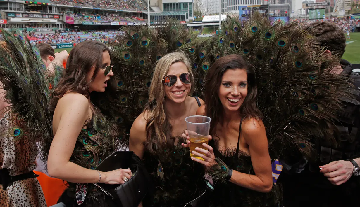 Tiga fans wanita mengenakan kostum burung merak saat menyaksikan pertandingan RugbY Sevens di Hong Kong (8/4). Para wanita yang  ini hadir mengenakan pakaian dan atribut unik demi mendukung tim kesayangannya. (AP Photo / Kin Cheung)