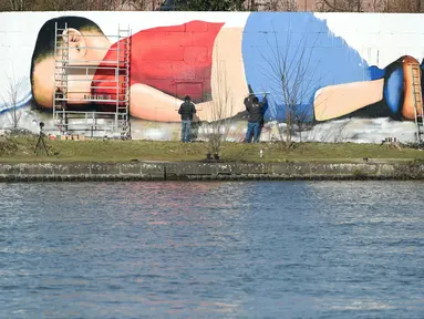 Seniman melukis mural bergambar balita Aylan Kurdi yang meninggal karena tenggelam di dinding pinggiran sungai di Frankurt, Jerman, 9 Maret 2016. Gambar tersebut dibuat untuk menarik simpati pengendara, wisatawan dan dunia. (Arne Dedert/dpa/AFP)