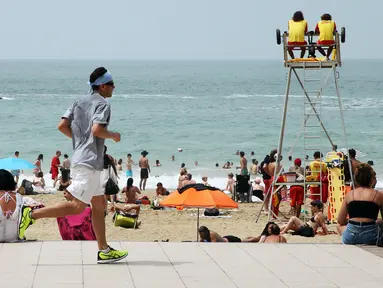 Seorang pria joging saat orang-orang menikmati pantai dekat Samudra Atlantik di Biarritz, Prancis, 14 Juni 2022. Cuaca panas diperkirakan akan berlangsung selama beberapa hari di seluruh Prancis. (AP Photo/Bob Edme)