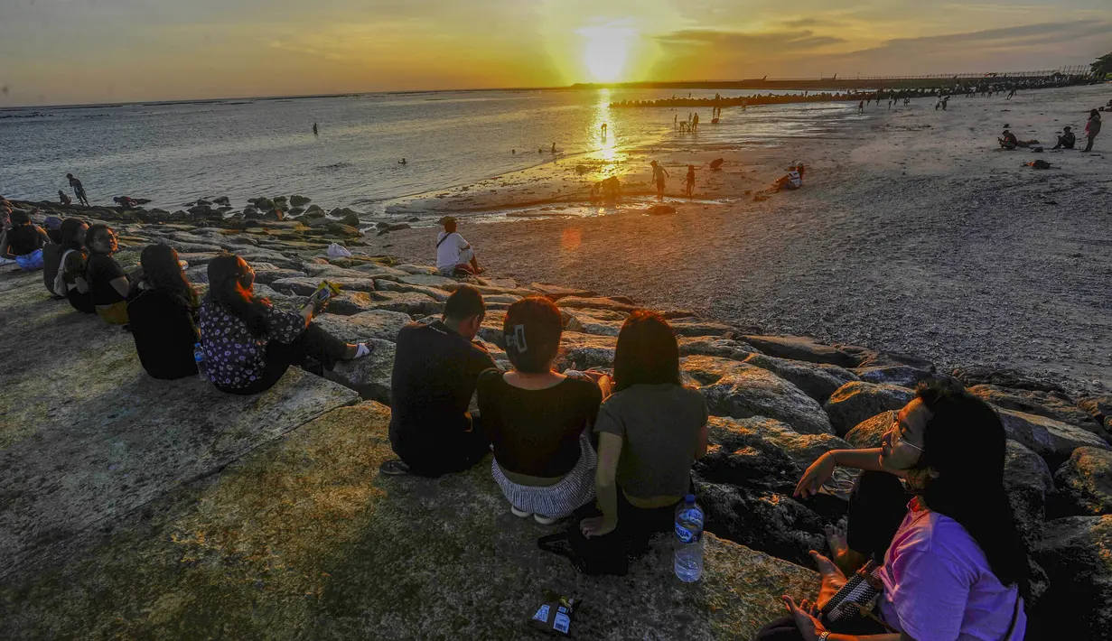 Pantai Kelan menawarkan pemandangan senja yang dramatis. Saat matahari perlahan tenggelam, langit berubah oranye keemasan dan berpadu dengan siluet pesawat yang tengah lepas landas atau mendarat. Kombinasi inilah yang menciptakan pengalaman visual unik dan jarang ditemukan di pantai lain. Tampak dalam foto, aktivitas wisatawan menikmati waktu senja di Pantai Kelan, Badung, Bali. (merdeka.com/Arie Basuki)