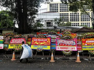 Pemulung berjalan melewati karangan bunga di depan Gedung KPU, Jakarta, Sabtu (21/4). Karangan bunga di depan Gedung KPU terus bertambah setiap harinya. (Liputan6.com/JohanTallo)