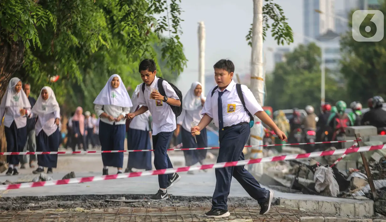 Pelajar melintasi trotoar yang sedang direvitalisasi di kawasan Kramat Raya, Jakarta, Rabu (6/11/2019). Revitalisasi trotoar menyebabkan para pejalan kaki harus berjalan di pinggir jalan dan bersinggungan dengan sepeda motor. (Liputan6.com/Faizal Fanani)