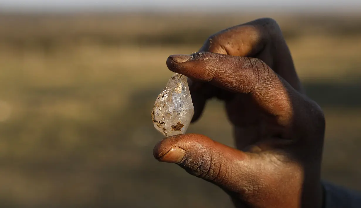 Anak laki-laki memegang apa yang dia yakini sebagai berlian setelah penemuan batu tak dikenal di desa KwaHlathi, luar Ladysmith, Afrika Selatan (15/6/2021). Lebih dari 1.000 orang berbondong-bondong mendatangi tanah luas di Desa KwaHlathi untuk mencari batu yang diyakini berlian. (AFP/Phill Magakoe)