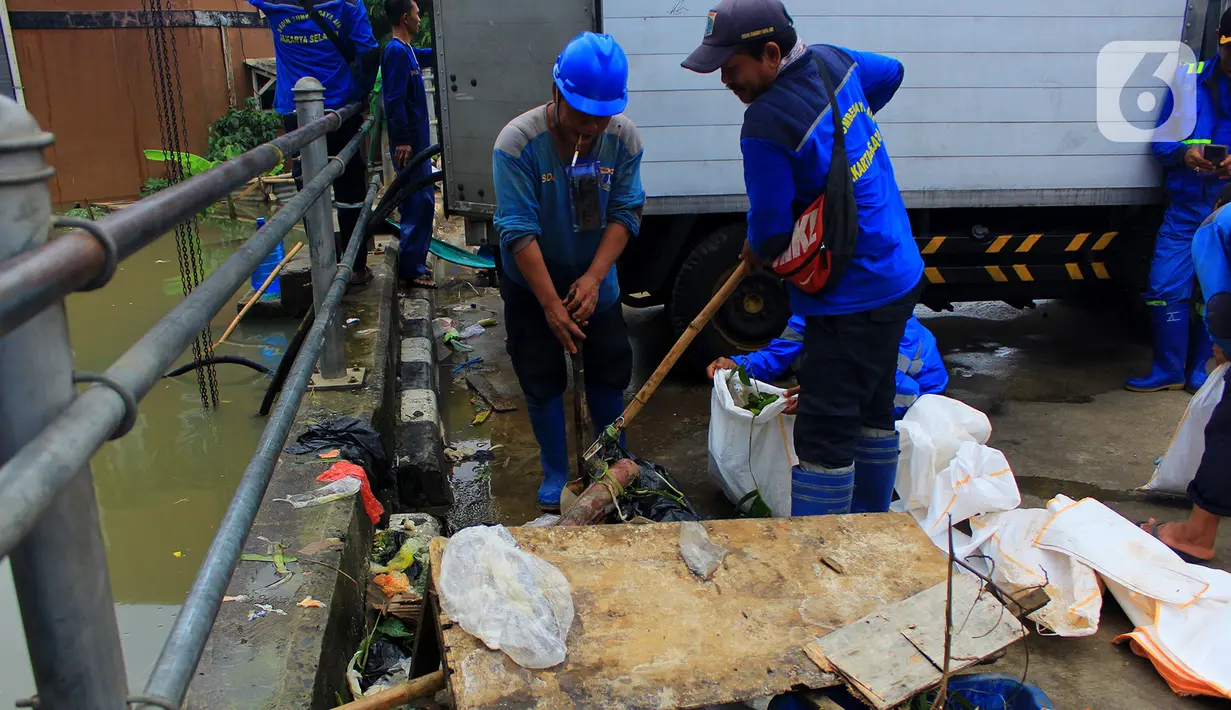 Petugas Sudin Sumber Daya Air (SDA) memunguti sampah-sampah yang tergenang saat banjir di kawasan Kampung Melayu Kecil, Bukit Duri, Jakarta, Selasa (25/2/2020). Banjir tersebut akibat luapan sungai Ciliwung. (merdeka.com/magang/ Muhammad Fayyadh)