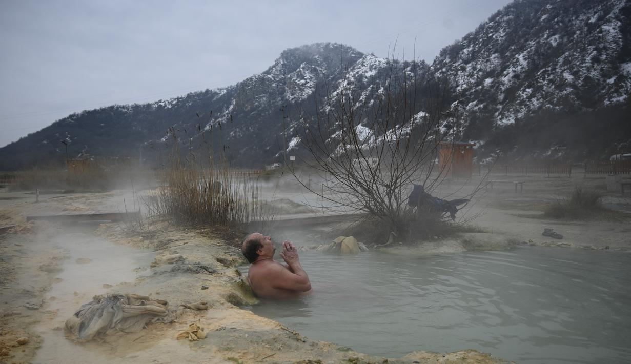 Seorang pria menikmati air panas di mata air mineral alami pada hari musim dingin di dekat desa Rupite, Bulgaria (2/2/2022). Penduduk setempat percaya bahwa air mineral menyembuhkan banyak penyakit dan gangguan. (AFP/Nikolay Doychinov)
