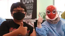 Seorang anak berpose dengan petugas medis yang mengenakan topeng superhero usai mengikuti vaksinasi kedua di Gedung  OJK, Jakarta, Minggu (16/01/2022). Bertemakan superhero untuk menghilangkan stigma menakutkan bagi anak-anak. (Liputan6.com/Angga Yuniar)