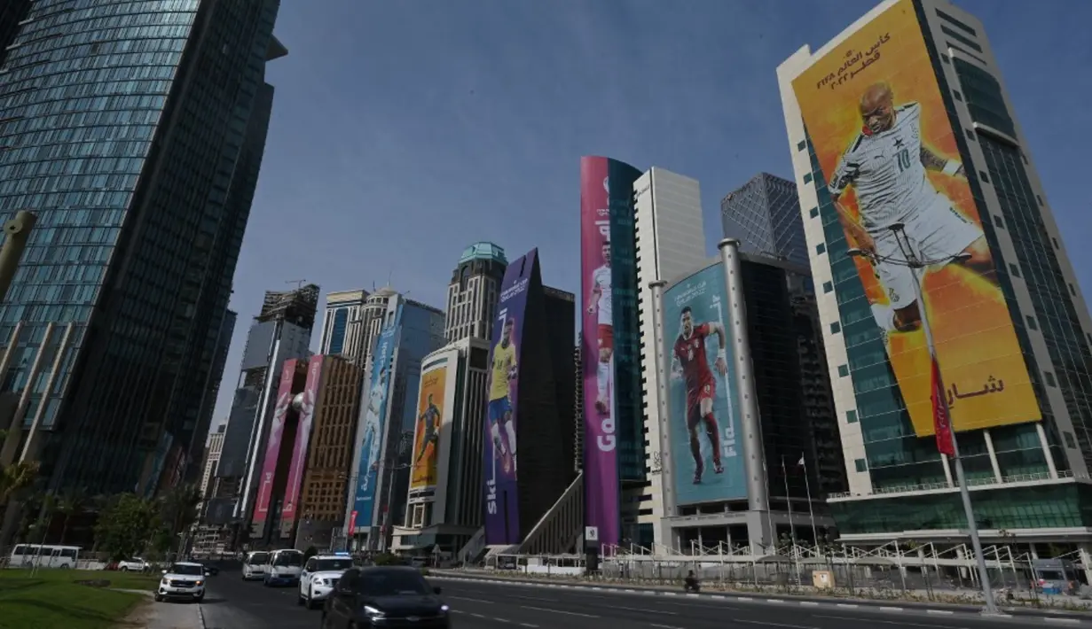 <p>Pengemudi berkendara melewati gedung-gedung yang dihiasi dengan gambar pemain sepak bola jelang Piala Dunia 2022 di Doha, Qatar, Minggu (6/11/2022). Piala Dunia 2022 akan dimulai pada 20 November 2022 hingga 18 Desember dengan menampilkan pertandingan pembuka antara tuan rumah Qatar vs Ekuador pada 20 November 2022. (Gabriel BOUYS/AFP)</p>