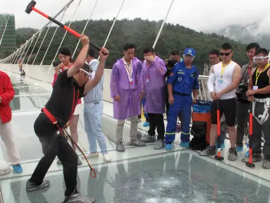 Seorang pria memukulkan palu untuk mencoba kekuatan kaca yang dipakai untuk jembatan di Provinsi Hunan, Cina, (25/6). Jembatan sepanjang 430 meter tersebut terbuat dari bahan kaca. (REUTERS / Jimmy Guan)