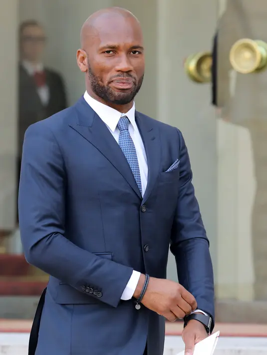 Didier Drogba saat tiba menghadiri undangan makan siang Presiden Liberia George Weah dan Presiden Prancis Emmanuel Macron di Istana Elysee di Paris, (21/2). Mantan penyerang Chelsea ini tampil dengan setelan jas berwarna biru. (AFP Photo/Ludovic Marin)