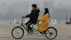 Pasangan naik sepeda menggenakan masker saat pemandangan kota diselimuti kabut tebal partikel debu halus di Seoul, Korea Selatan (5/3). Kementerian Lingkungan Korsel mengeluarkan langkah-langkah penurunan debu halus darurat. (AP Photo/Ahn Young-joon)