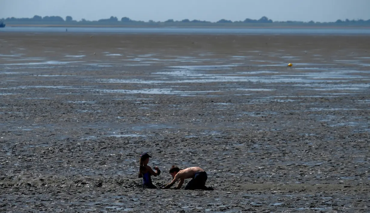 Anak-anak bermain lumpur saat suhu mencapai 34 derajat Celcius di dekat pantai Laut Utara di Wremen, Jerman barat (24/7/2019). Peramal cuaca memprediksi suhu tertinggi di seluruh Eropa barat yang terkena gelombang panas akan mencetak rekor suhu terbaru.  (AFP Photo/Patrik Stollarz)