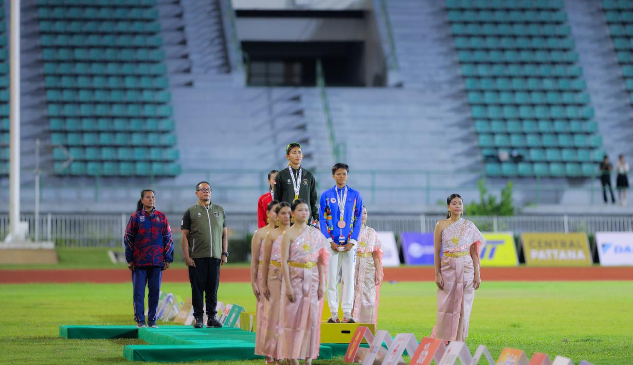 Raihan ini setelah Emilia Nova berhasil mengumpulkan total 5.497 poin sekaligus mengakhiri penantian panjangnya di nomor tersebut. Tampak dalam foto, atlet atletik Indonesia, Emilia Nova (tengah) saat prosesi penghormatan bendera usai memenangi lomba dan meraih emas nomor heptathlon (tujuh lomba) SEA Games 2025 di Stadion Supachalasai Bangkok, Thailand Selasa (16/12/2025) malam. (Bola.com/Bagaskara Lazuardi)