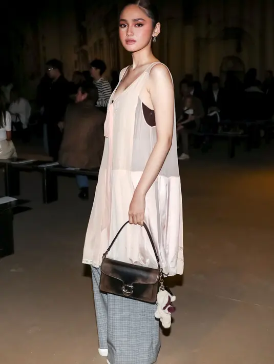 Dari Indonesia, Syifa Hadju tampil memikat dengan Pleated Bow Dress berwarna blush pink yang dipadukan dengan celana wide-leg bermotif abu-abu. Look ini semakin manis berkat tas Tabby Loved Leather yang khas dengan efek autentik, serta bag charm berbentuk gajah yang whimsical. Soho Sneakers klasik menyempurnakan gaya femininnya yang tetap kasual.