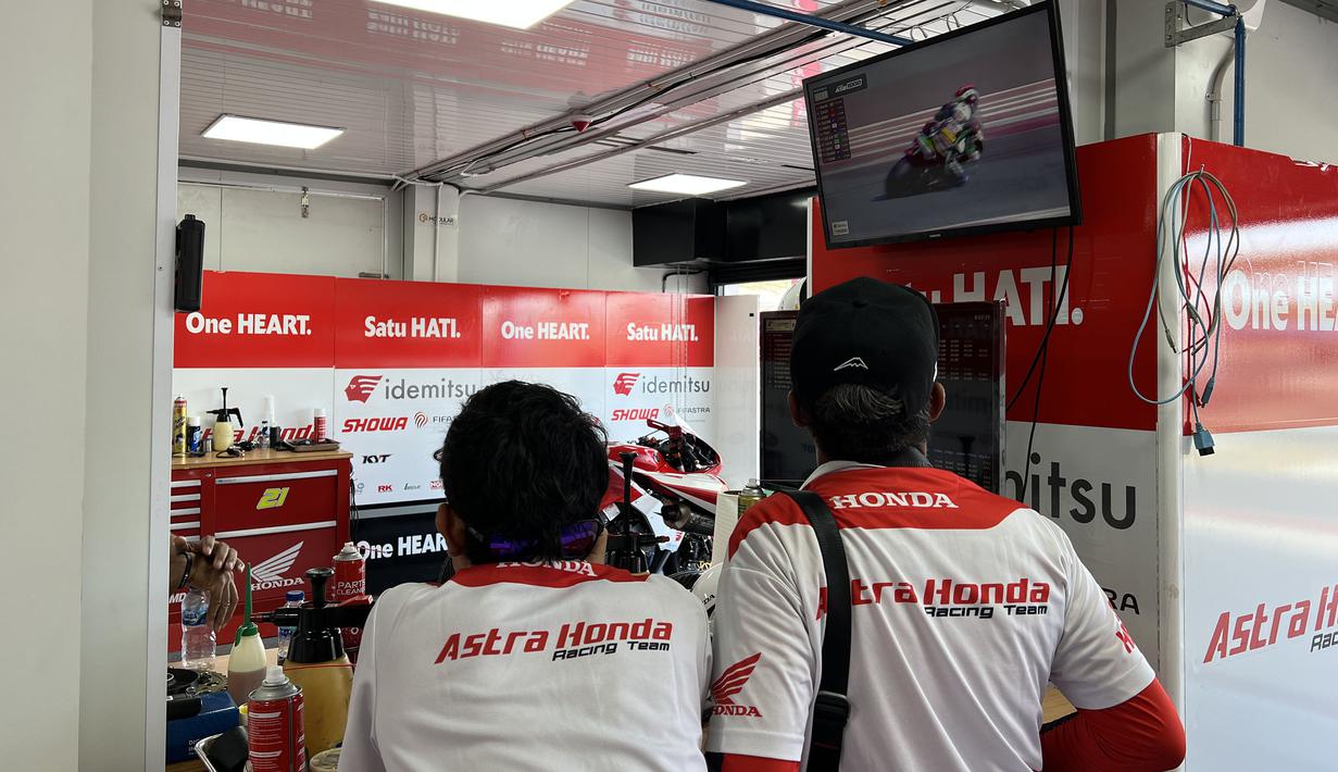 Dua orang mekanik Astra Honda Racing Team (AHRT) menyaksikan rekaman balapan dari televisi di sela mempersiapkan motor pembalapnya yang akan bertarung di balapan hari kedua ARRC Mandalika 2023 di Sirkuit Mandalika, Lombok, Sabtu (12/8/2023). (Bola.com/Iqri Widya)