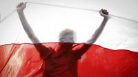 Demonstran digambarkan siluet oleh bendera nasional Belarusia tua saat unjuk rasa di Minsk, Belarus, Minggu (4/10/2020). Ratusan ribu warga Belarusia telah melakukan protes setiap hari sejak 9 Agustus pemilihan presiden. (AP Photo)