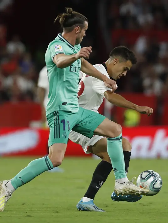 Gelandang Real Madrid, Gareth Bale berusaha merebut bola dari pemain Sevilla Sergio Reguilon pada pertandingan lanjutan La Liga Spanyol di stadion Ramon Sanchez Pizjuan di Seville (22/9/2019). Real Madrid menang tipis atas Sevilla 1-0. (AP Photo/Miguel Morenatti)