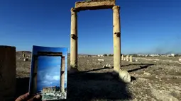 Fotografer bernama Joseph Eid memegang foto Temple of Baal Shamin yang diambil pada tanggal 14 Maret 2014 di depan sisa-sisa kuil bersejarah setelah dihancurkan oleh ISIS pada September 2015 di kota kuno Palmyra, Suriah, 31 Maret 2016. (Joseph EID/AFP)