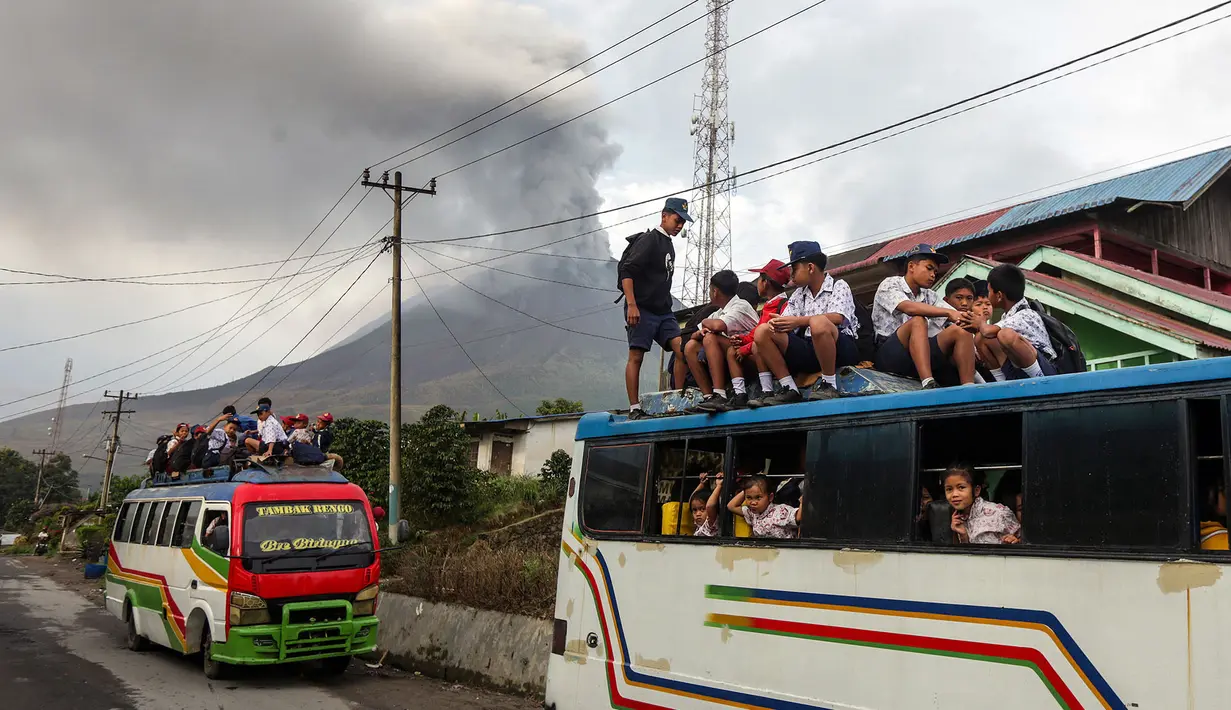 Anak-anak berangkat sekolah a dengan latar belakang Gunung Sinabung yang menyemburkan abu dan asap tebal, sebagaimana terlihat dari Karo, Provinsi Sumatra Utara, Rabu, 2 September 2026. (AFP/ YT Haryono)