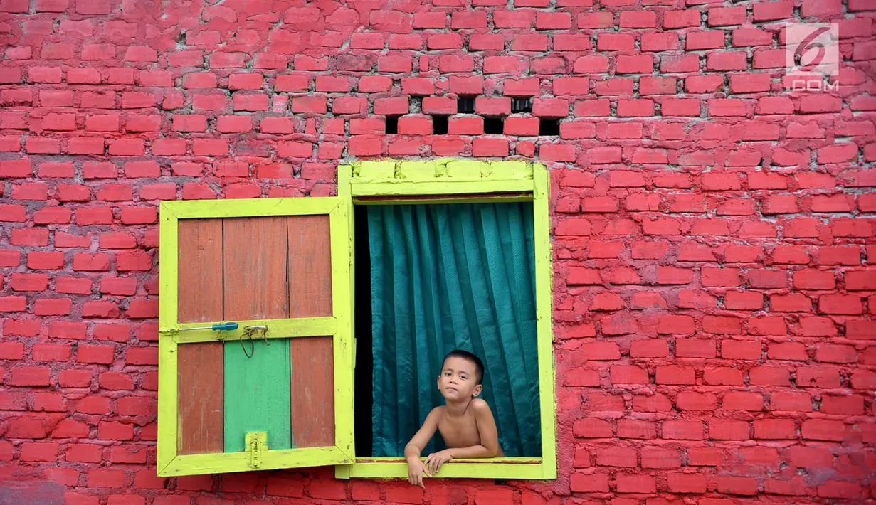 Seorang bocah melongok keluar jendela di Kampung Warna Warni Lubuklinggau, Sumatera Selatan, Rabu (10/1). Kampung yang dulunya menjadi pusat perjudian, sabung ayam, dan lokasi transaksi narkoba itu kini telah berubah wajah (Liputan6.com/Immanuel Antonius)