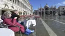 Orang-orang duduk di bar di St. Mark's Square yang terendam banjir di Venesia, Italia, Jumat (5/11/2021). Setelah Venesia mengalami banjir terparah kedua dalam sejarahnya pada November 2019, kota itu dibanjiri empat kali pasang luar biasa dalam waktu enam minggu. (AP Photo/Luigi Costantini)