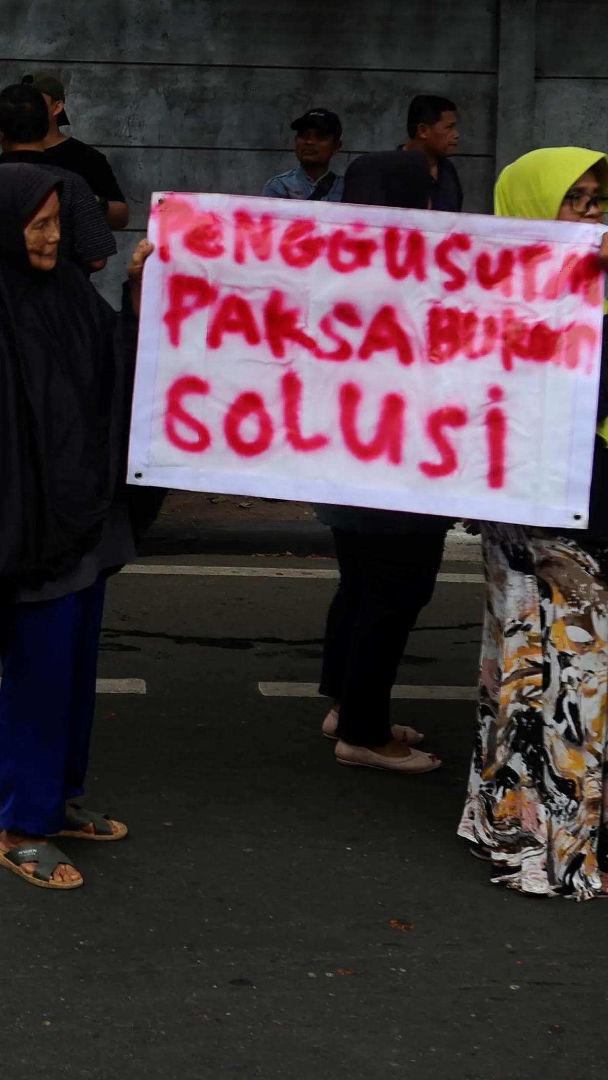 Demonstran ibu-ibu menunjukkan poster bertuliskan "Penggusuran Paksa Bukan Solusi" saat beraksi.