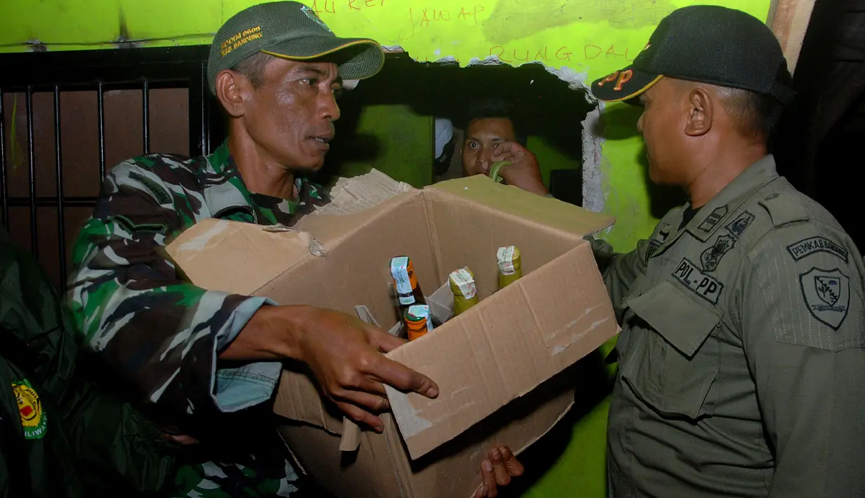 Petugas membawa kardus berisi miras oplosan saat penggerebekan di Cicalengka, Bandung, Minggu (8/4).  Pasca meninggalnya 15 orang akibat menenggak miras oplosan, petugas melakukan penggerebekan tempat penjualan dan pembuatan miras. (Timur Matahari/AFP)