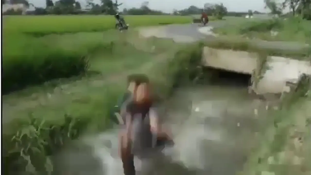 terlihat tiga orang pemuda jatuh ke dalam selokan karena pengendara motor tak mampu mengendalikan kendaraannya saat hendak menikung.