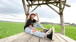 Palantun lagu "Gulu Pedot" ini berhasil beberapa kali trending di YouTube dengan musik videonya. Penampilannya tetap stylish saat berfoto di area sawah. Menggunakan bucket hat berwarna putih, baju kaus hitam dan celana jeans berwarna terang melengkapi gayanya. (Liputan6.com/IG/@esaristyyy_)