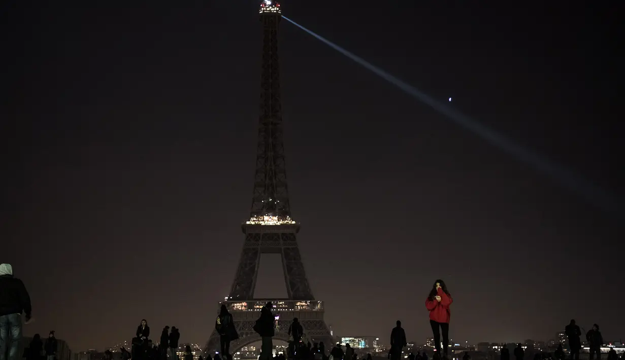 Sejumlah pengunjung berkumpul di dekat Menara Eiffel yang mengalami pemadaman sementara di Paris, Rabu (14/12). Pemadaman lampu Menara Eiffel ini sebagai simbol keprihatinan terhadap korban di Aleppo, Suriah. (AFP PHOTO/PHILIPPE LOPEZ)