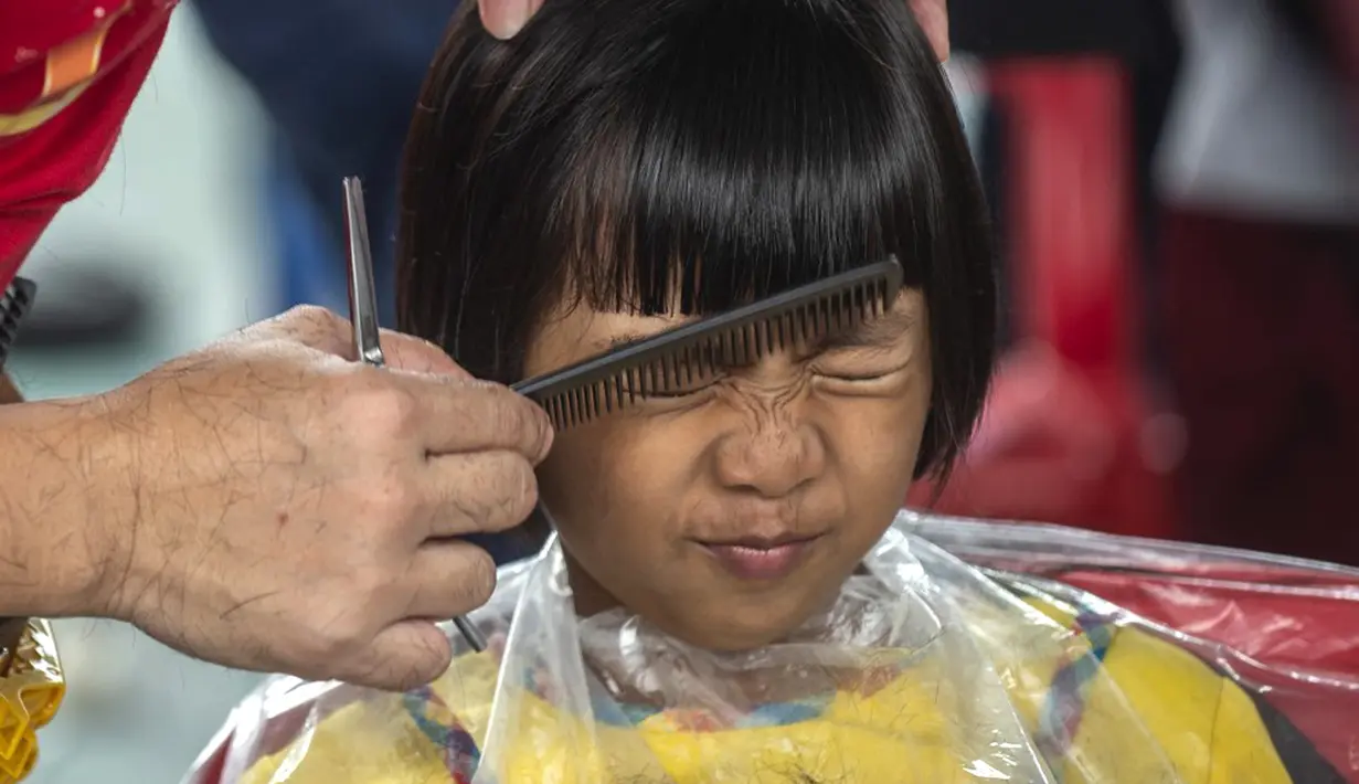 Seorang anak mengikuti cukur rambut gratis saat acara amal di Surabaya, Jawa Timur, Senin (8/11/2021). Layanan cukur rambut gratis ini dilakukan kepada 100 anak yatim piatu. (Juni Kriswanto/AFP)