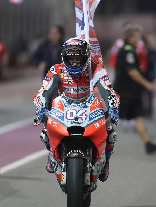 Pembalap Ducati Andrea Dovizioso mengendarai motornya sambil membawa bendera usai memenangkan balapan MotoGP Qatar 2018 di Sirkuit Internasional Losail (18/3). Andrea Dovizioso sukses memenangi seri pembuka MotoGP 2018 di Qatar. (AFP Photo/Karim Jaafar)