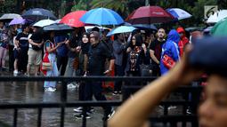Penonton mengenakan payung karena hujan saat mengantre tiket masuk konser Liam Gallagher di Ecovention Ancol, Jakarta Utara, Minggu (14/1). Liam Gallagher siap menghibur para penggemarnya selama 90 menit. (Liputan6.com/JohanTallo)