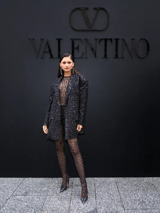 Zendaya mencuri perhatian saat hadir di show Valentino dengan outfit bernuansa hitam. Zendaya mengenakan gaun transparan dengan detail jaring-jaring yang dipadukan dengan short pants dan sequin blazer. (Valentino)