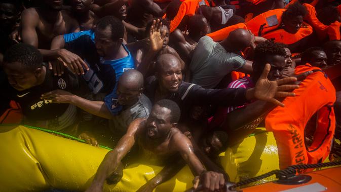 Imigran Afrika meminta jaket pelampung saat diselamatkan oleh kapal bermisi kemanusiaan milik LSM Spanyol di tengah Laut Mediterania, lepas pantai Libya, Selasa (25/7). Petugas menemukan 13 jasad di atas perahu karet padat imigran itu. (AP/Santi Palacios)