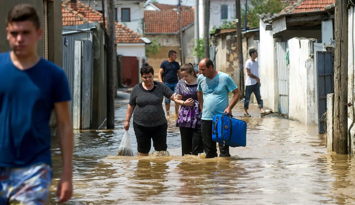 Sejumlah warga melewati jalanan yang banjir akibat hujan deras di Ibu Kota Skopje, Makedonia, Minggu (7/8). Pemerintah menyatakan keadaan darurat sehari setelah setidaknya 21 orang tewas dalam banjir bandang yang disebabkan badai. (Robert ATANASOVSKI/AFP)