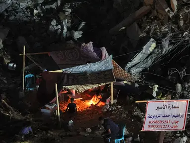 Warga Palestina duduk di tenda yang didirikan di atas reruntuhan bangunan yang hancur dalam serangan udara Israel di Kota Gaza (24/5/2021). Menyusul gencatan senjata yang dicapai setelah perang 11 hari antara Israel dan Hamas, Warga Palestina mendirikan tenda di reruntuhan. (AFP/Mohamed Abed)