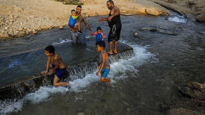 Warga Palestina meluncur di kanal air yang digunakan untuk irigasi untuk mendinginkan tubuh saat suhu udara mencapai 44 derajat Celcius di kota Jericho, Tepi Barat (1/9/2020). (AFP Photo/Ahmad Gharabli)