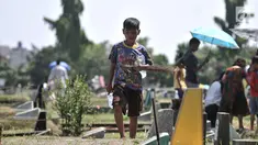 Seorang anak membawa sapu lidi dan botol kosong usai membersihkan salah satu makam di TPU Penggilingan, Pulogadung, Jakarta, Kamis (10/5). Tradisi ziarah jelang Ramadan menjadi berkah bagi anak-anak pembersih makam. (Merdeka.com/Iqbal S. Nugroho)
