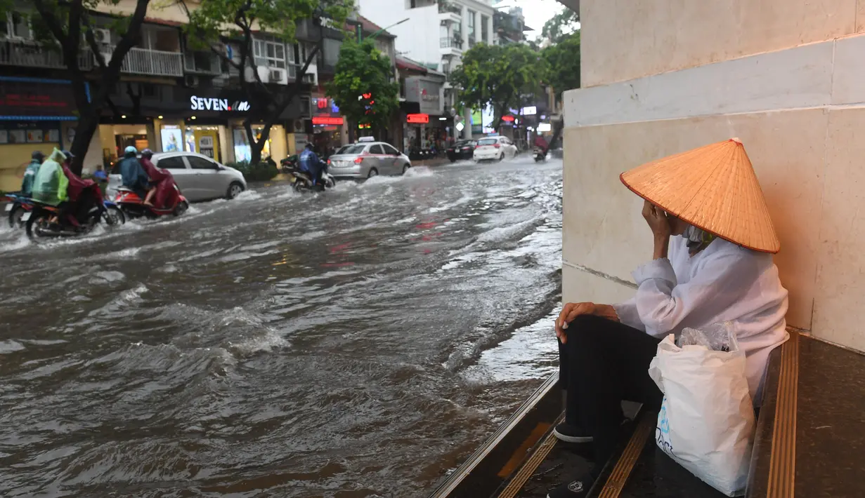Seorang wanita menunggu hujan di sepanjang jalan yang banjir setelah badai tropis Talas terjadi di Hanoi, Vietnam utara (17/7). (AFP Photo/Hoang Dinh Nam)