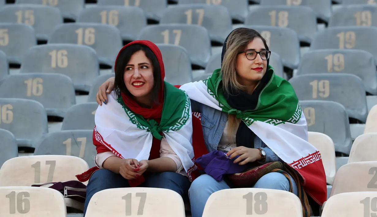 Wanita Iran mengenakan bendera negara mereka saat menyaksikan laga kualifikasi Piala Dunia 2022 antara Iran dengan Kamboja di Stadion Azadi, Teheran, Iran, Kamis (10/10/2019). Ini merupakan pertama kalinyqa wanita Iran boleh menonton bola dalam stadion sejak tahun 1981. (AP Photo/Vahid Salemi)