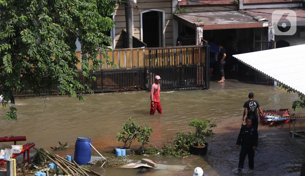 Warga melintasi banjir akibat jebolnya tanggul karena tertimpa tanah longsor, di Perumahan Nerada Estate Ciputat, Tangerang Selatan, Sabtu (12/6/2021). Longsor yang menimpa sejumlah rumah membuat tanggul pembatas kali jebol dan air meluap sehingga menyebabkan banjir. (Liputan6.com/Angga Yuniar)
