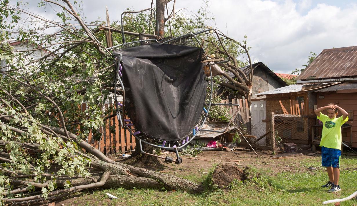 Seorang anak melihat trampolinnya tergantung di atas pohon akibat tornado di Lachute, Quebec, Rabu (23/8). Tornado ini adalah yang keenam dalam setahun terakhir di Quebec dengan skala yang lebih tinggi. (Ryan Remiorz/The Canadian Press via AP)